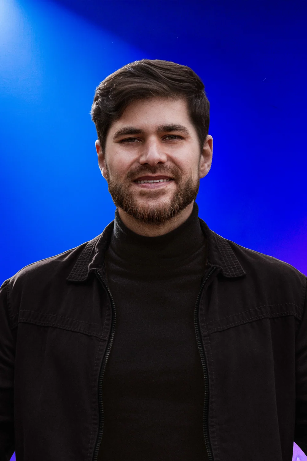 Iury Santos sorrindo, de frente, sob luz azul e violeta